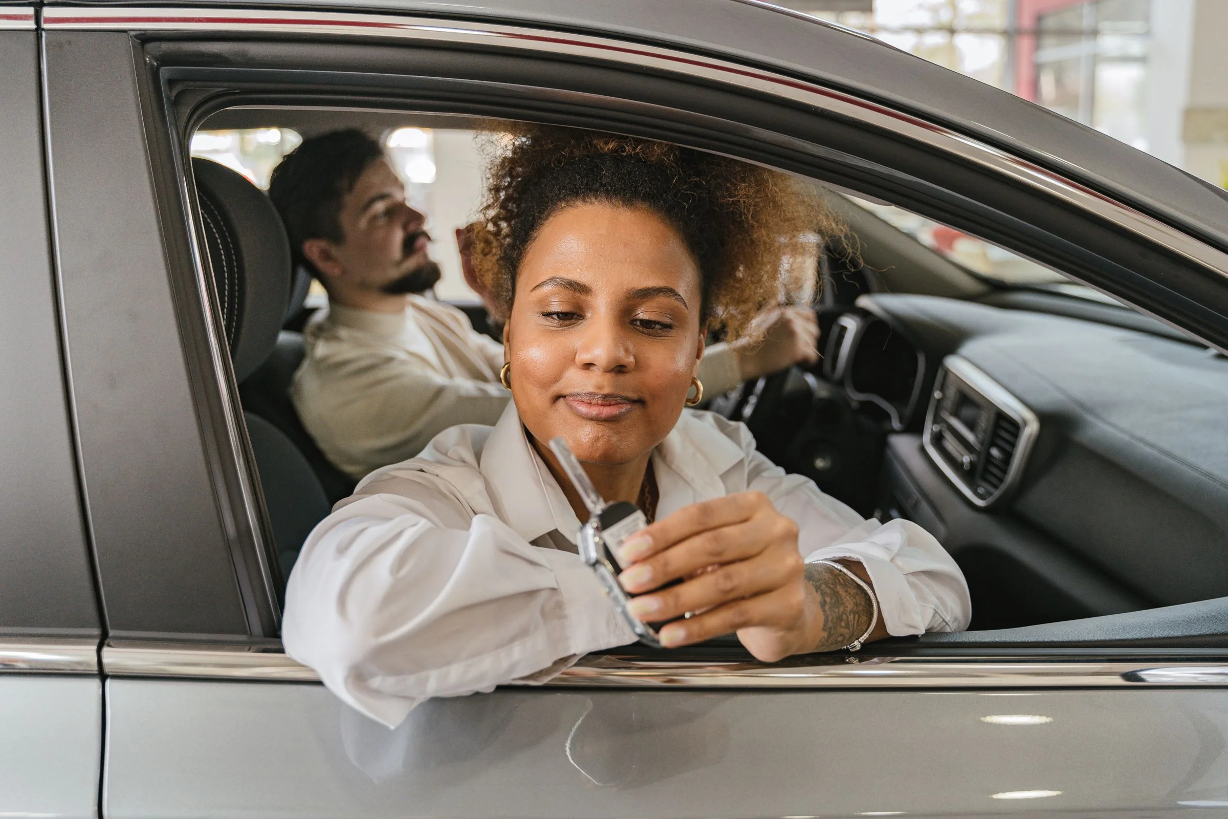 Zwei Menschen im Auto, eine Frau hält die Fahrzeugschlüssel – Symbolbild